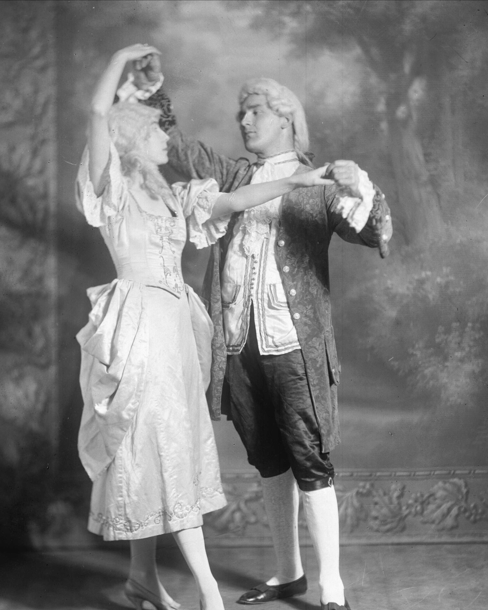 Gustav Borgen, Gruppeportrett, frøken Kitty Normann danser med en mann, begge kledd i 1700-talls kostyme.