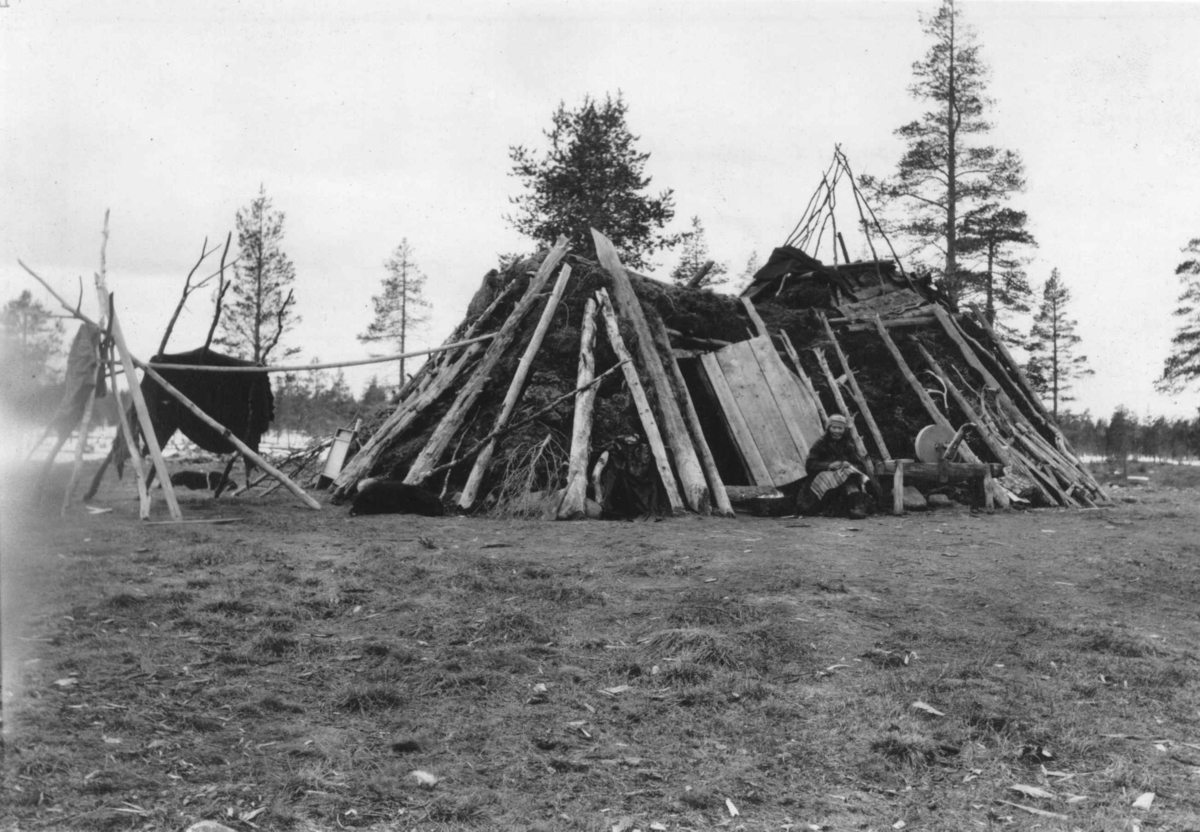 Konrad Nielsen, Gamme med oppbygging for anbringelse av vindskjerm over røkhullet, foran inngangen sitter en kvinne ved siden av en slipestein. Laksefjord.