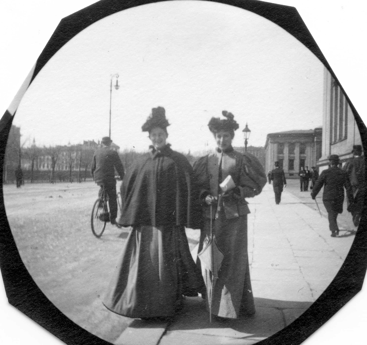 Fredrik Carl Mülertz Størmer, To damer spaserer langs Karl Johans gate, Oslo, på fortau utenfor Universitetet, Oslo. Syklist på vei i retning Slottet.