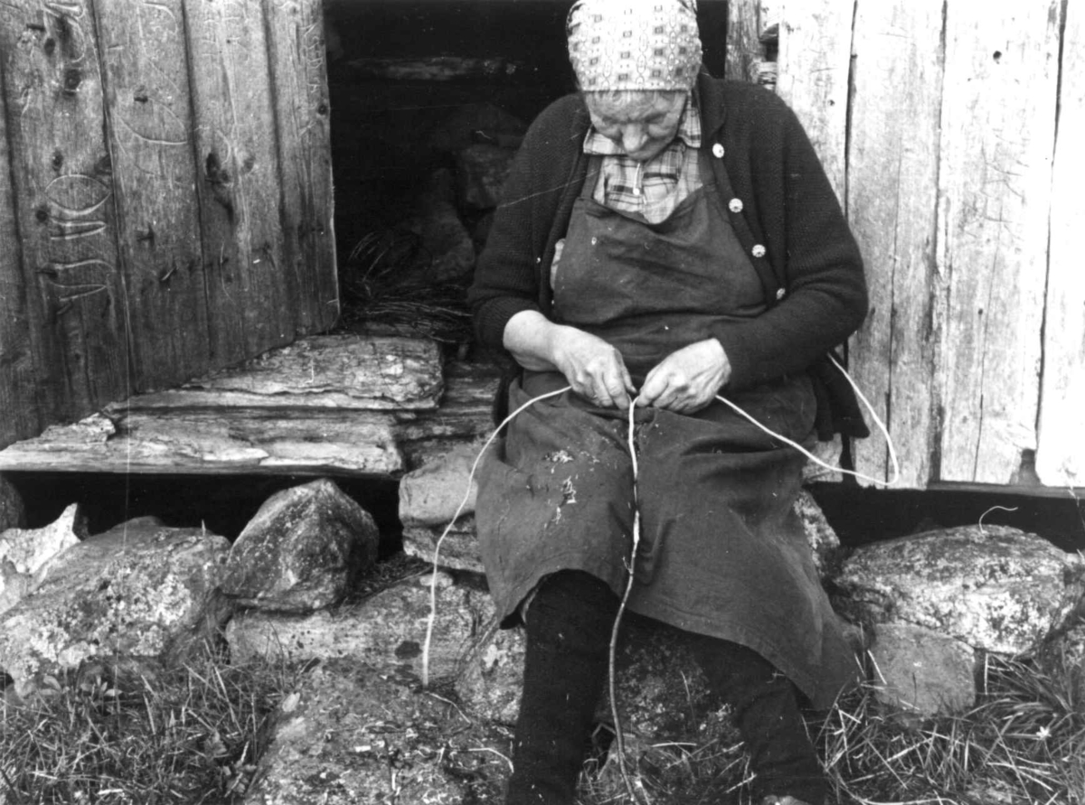Anna Grostøl, Frøysnes, Bygland, Setesdal, Aust-Agder 1941. Fru Gyro sitter på en stein utenfor et hus og kløyver teger.