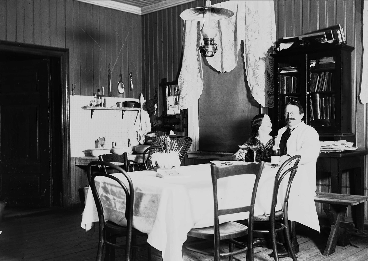Axel Quinsgaard Wiborg, Interiør med mann og kvinne, Axel Q. Wiborg med antatt sin kone Margrethe. Spisebord med vaskestell i bakgrunnen. Ukjent sted.