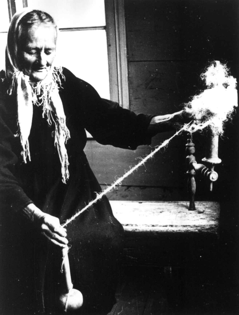 Anna Grostøl, Ragnhild Åvitsland spinner kutagl og grov ull på en liten hjemmelaget håndrokk i tre. Eiken, Hægebostad, Vest-Agder 1941.