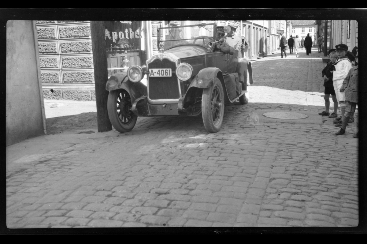 Rolf Sr. Sundt, Rolf Sundt Sr. kjører sin Buick gjennom ukjent gate. En gruppe smågutter er tilskuere. Finn Sundt er passasjer. Fotografert 1928.
