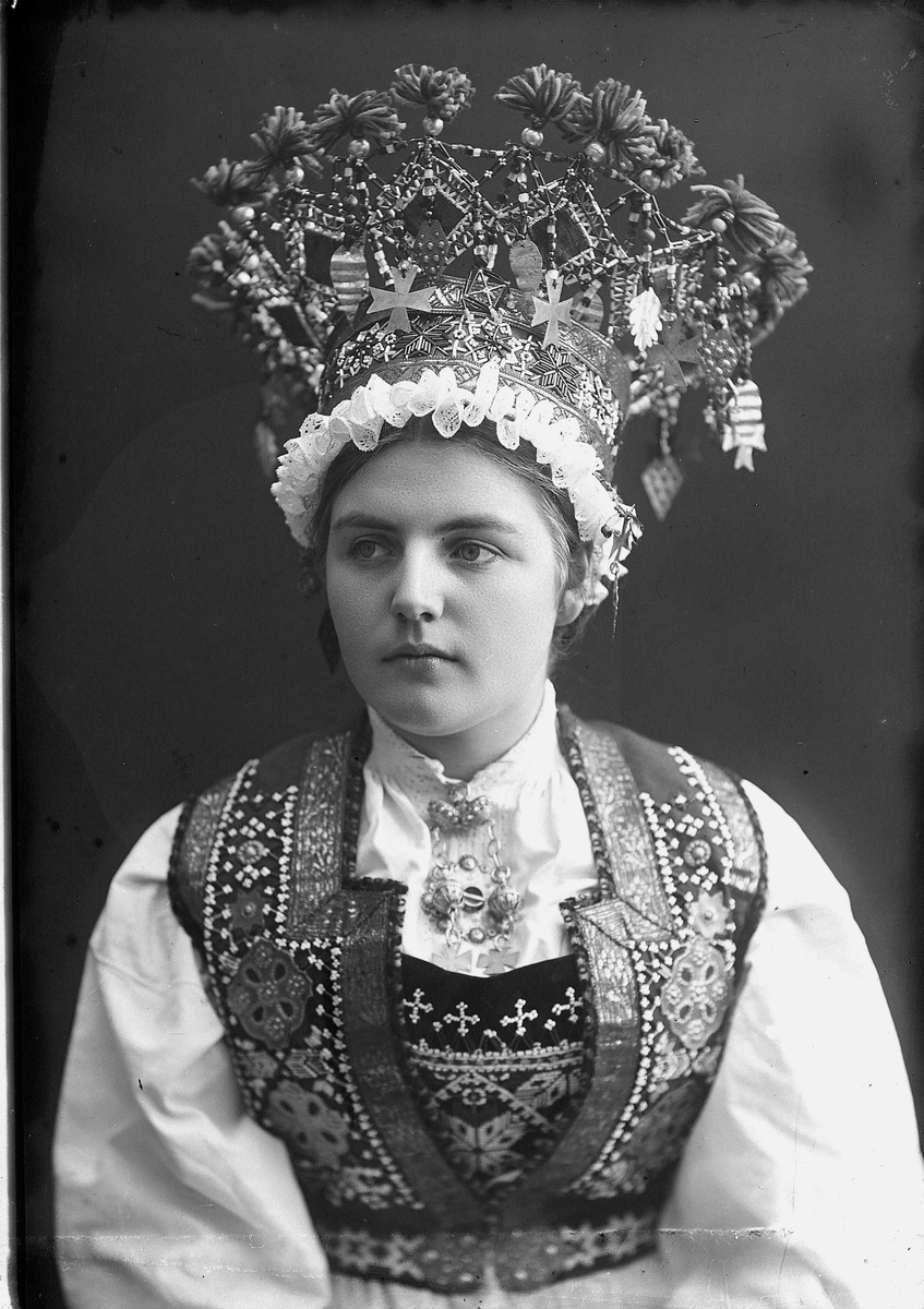 Solveig Lund, Studiofotografi av kvinne med brudedrakt og brudekrone fra Voss i Hordaland. Sittende. Bryst/hofteutsnitt. Frortalt vendt. Ser ut av bildet mot venstre.