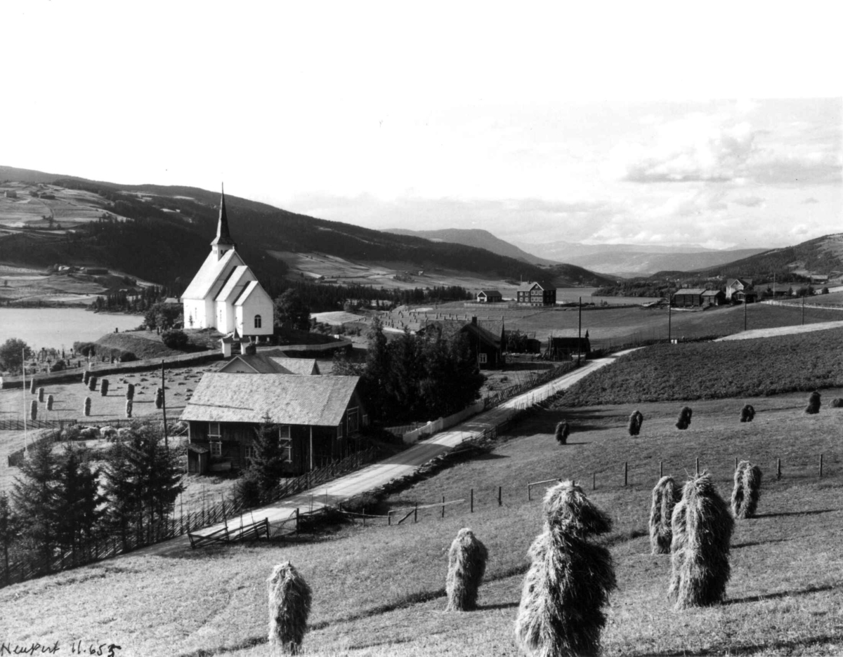 Hermann Christian Neupert, Ulnes kirke, Oppland 1934. Jordbruksbygd med gårdsanlegg. Skurdonn. Vei gjennom bygda. Omgitt av åser. Fjell i bakgrunnen.