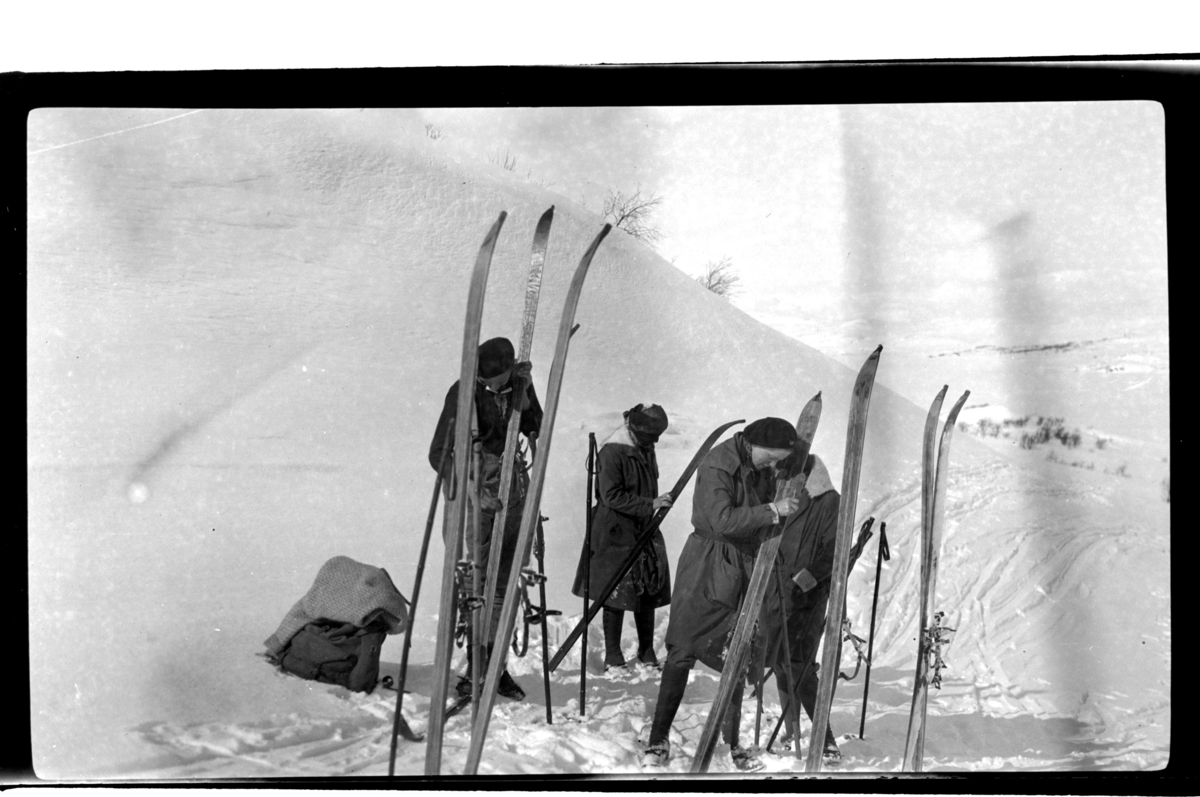 Rolf Sr. Sundt, Fire ukjente skiløpere smører ski i fjellandskap. Fotografert 1925.