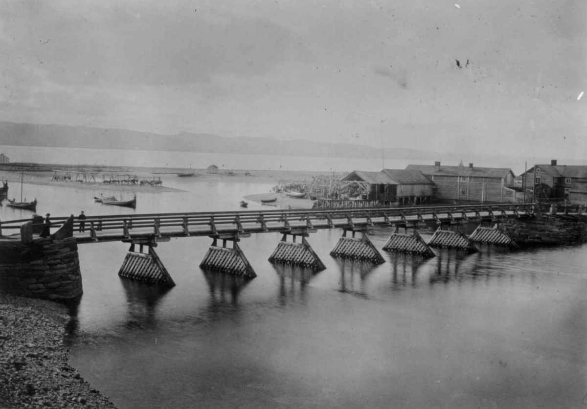 Ellisif Rannveig Wessel, Vestre Jakobselvs, første bro, bygget 1883-1885, Vadsø, Finnmark. Bygninger for enden av broen og båter på elven. Foto fra 1890-årene.