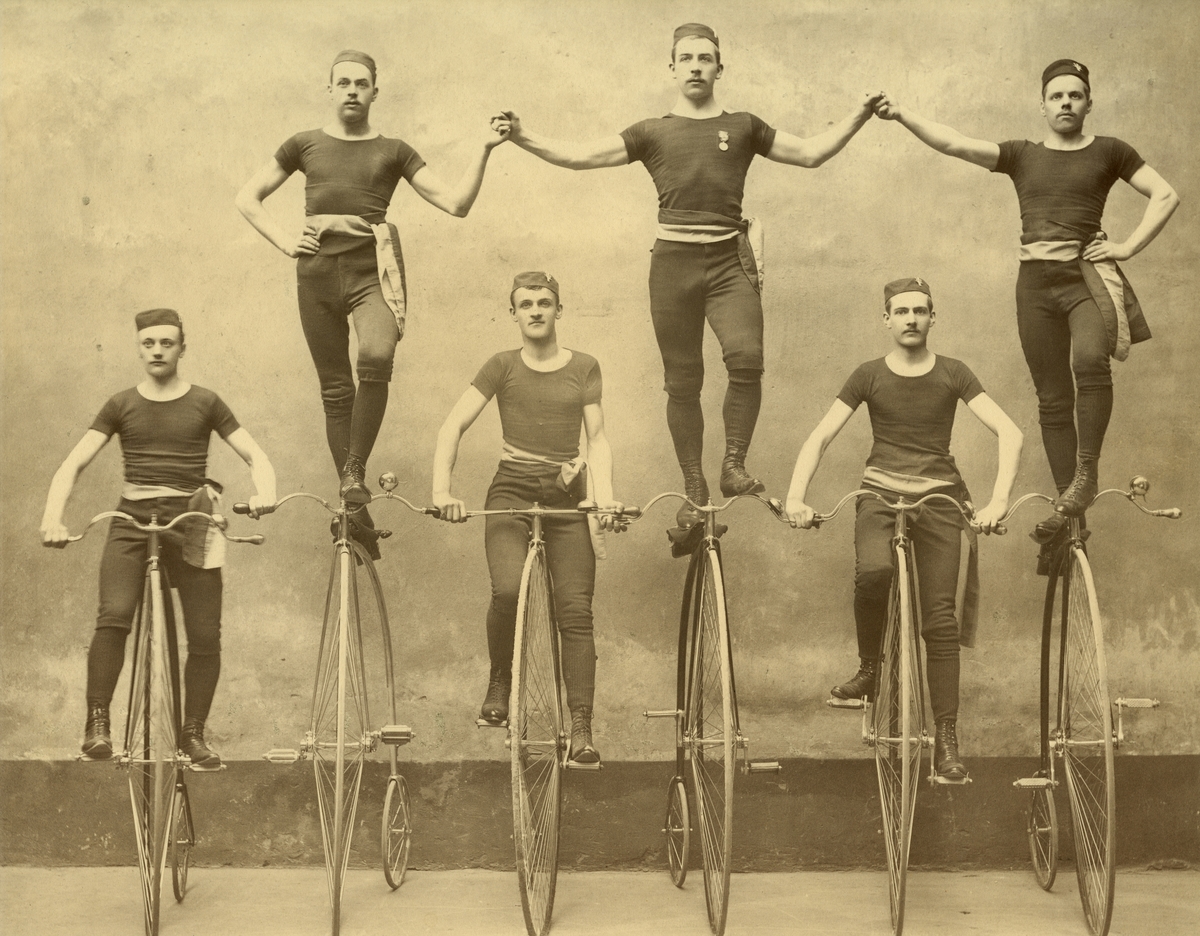 Unknown artist, Höghjulingar. Stockholms Bicycle Klubb vid en uppvisning omkring 1885. Byxor och tröja av trikå, snörkängor och blågult skärp var uppvisningsdräkten.