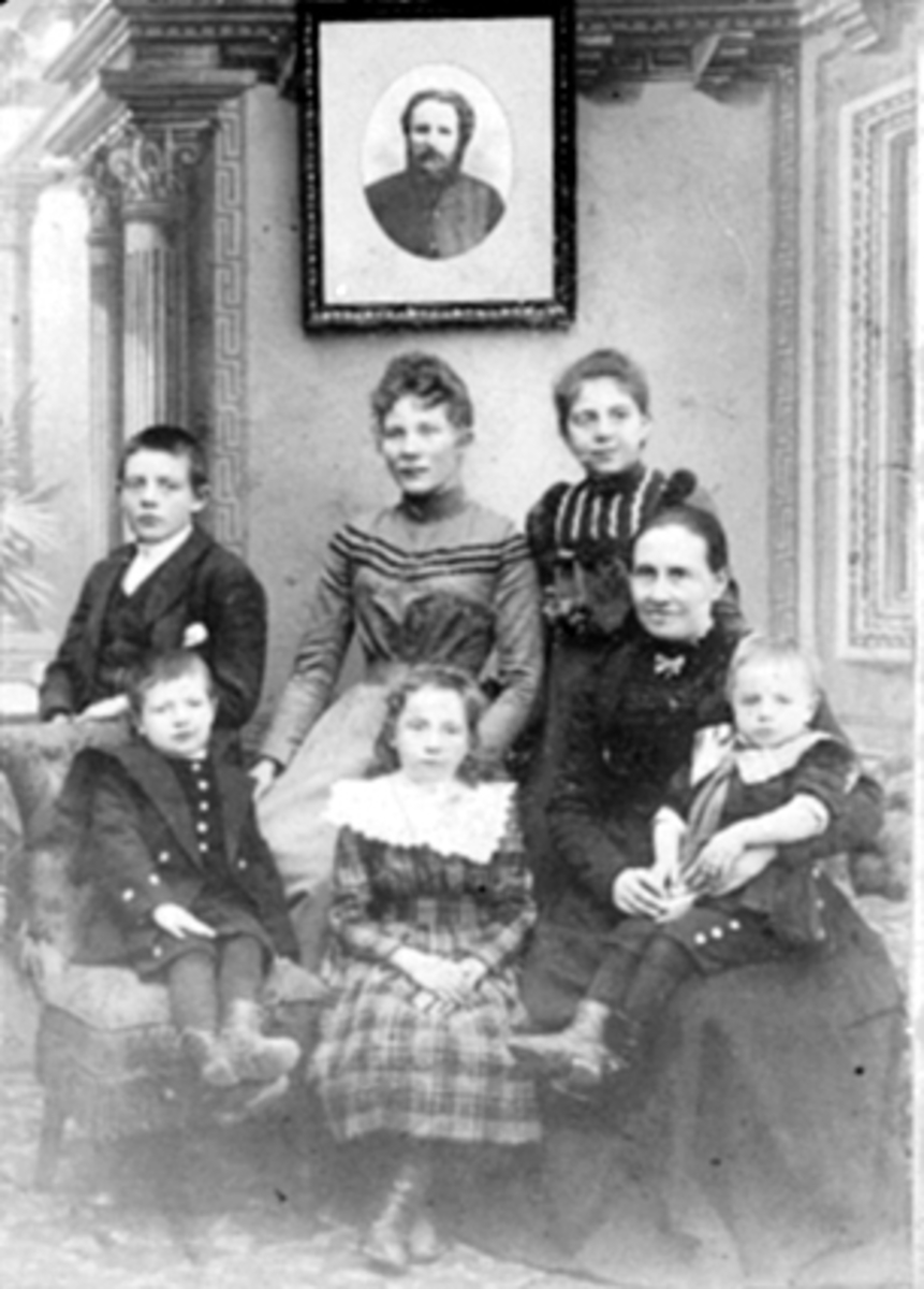 Anno Domkirkeodden, GRUPPE 7, FAMILIEN MELVOLD, BAK FRA VENSTRE: IVAR, KRISTINE (DATTER FRA FØRSTE EKTESKAP), ANNA, FORAN FRA VENSTRE: OLAV, MARIANNA, MARIE FØDT RUSTAD MED MARTIN PÅ FANGET. INTERIØR I FOTOSTUDIO MED PORTRETT AV KOMPONIST OG MUSIKER OLUF MELVOLD PÅ VEGGEN.