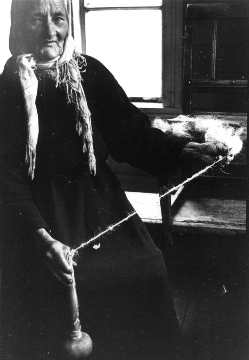 Anna Grostøl, Ragnhild Åvitsland spinner kutagl og grov ull på en liten hjemmelaget håndrokk i tre. Eiken, Hægebostad, Vest-Agder 1941.