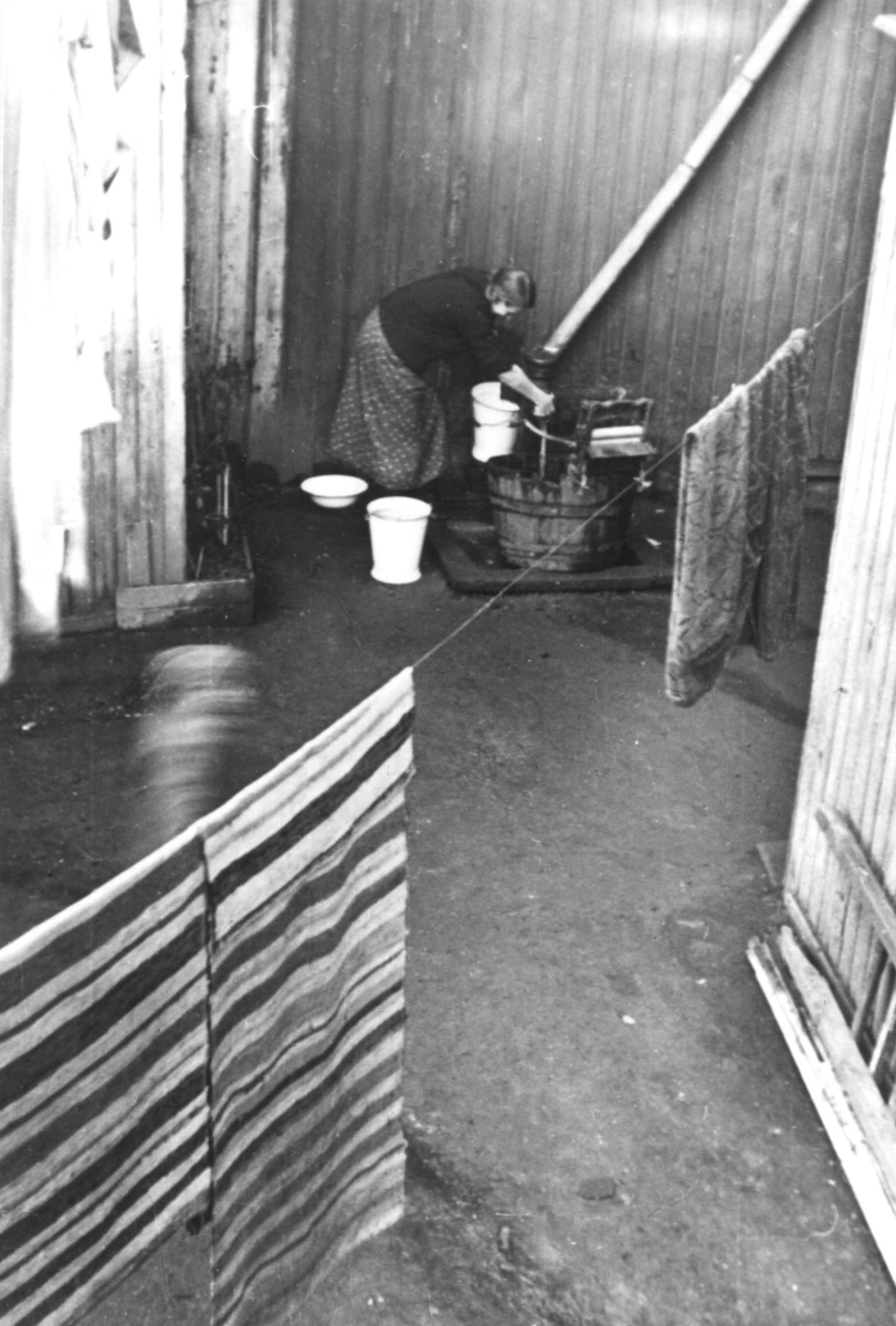 Nanna Broch, Klesvask, kvinne vasker tøy utendørs, utstyrt med vannpost, rulle/maskin til å presse ut vann, emaljerte bøtter og fat. Filleryer til tørk på snor. Jfr. NF.13400-072. Fra boliginspektør Nanna Brochs boligundersøkelser i Oslo 1920-årene.