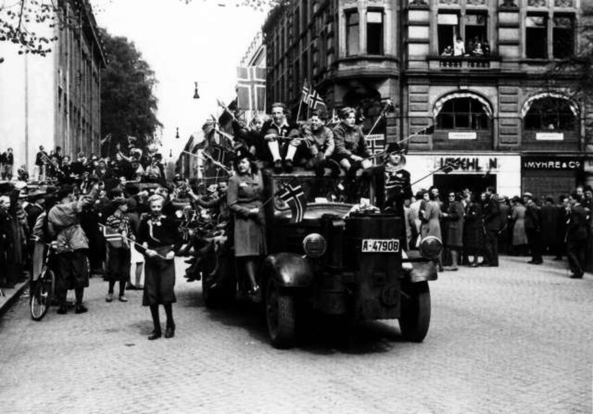 Anders Beer Wilse, Fra Oslo under fredsdagene i 1945. Lastebil med feirende ungdommer med flagg i krysset Karl Johans gate og Universitetsgata, med Landkreditgården i bakgrunnen.