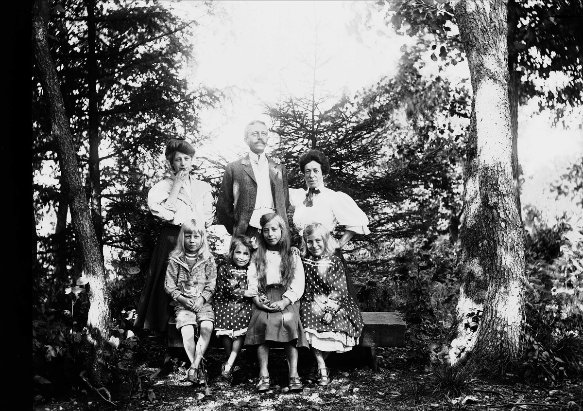 Axel Quinsgaard Wiborg, Familiegruppe, fire barn sitter på benk, en mann og to kvinner står bak, ukjent sted.