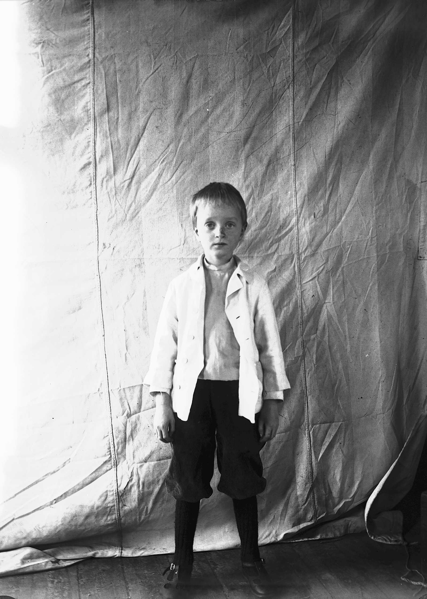 Axel Quinsgaard Wiborg, Portrett av gutt, fotografert mot opphengt bakteppe, ukjent sted. Antatt en av barna i familen Axel Q. Wiborg.