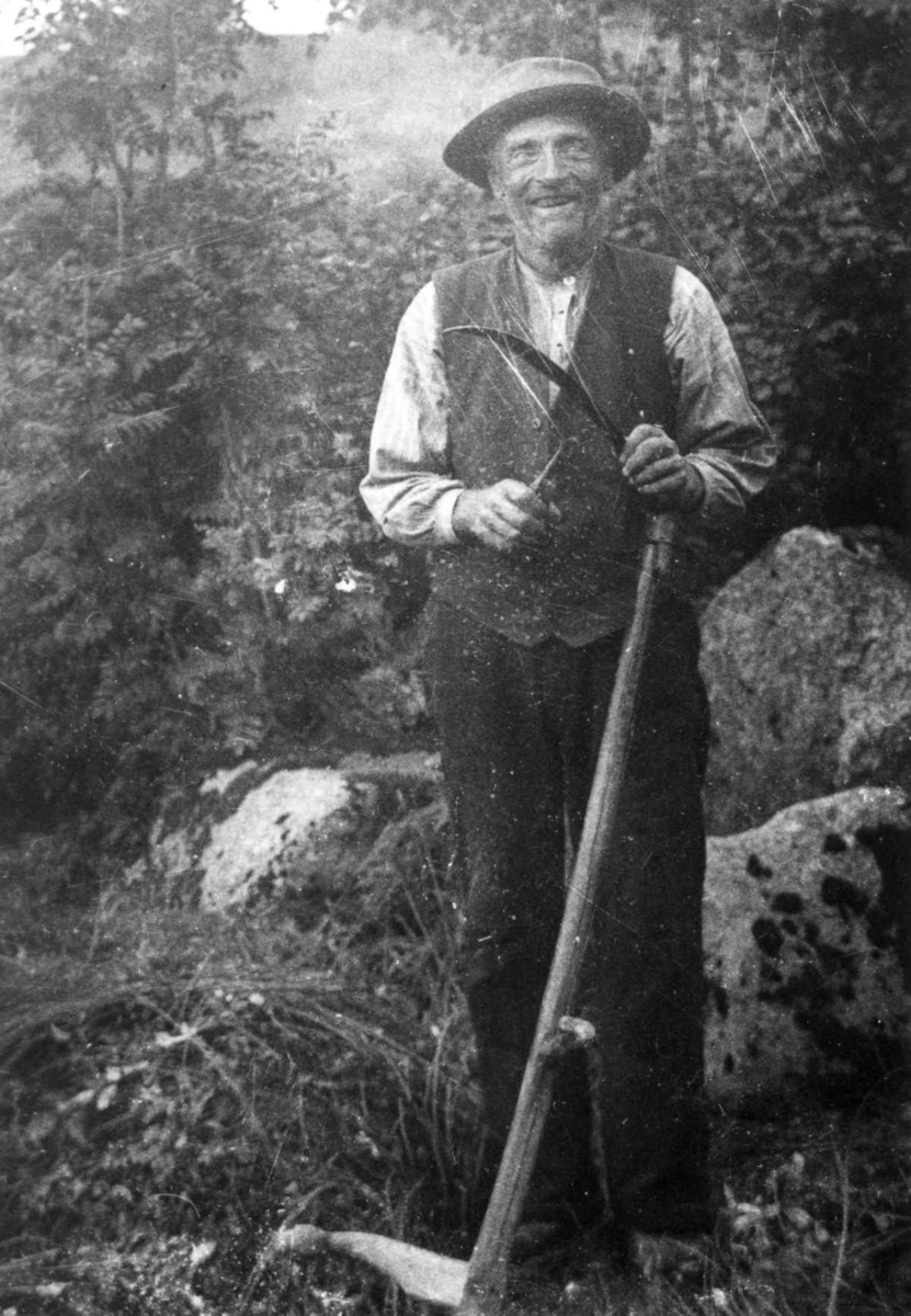 Anna Grostøl, Gunnleiv Håbbesland, født 1877, står ute og sliper ljåen. Eiken 1937.