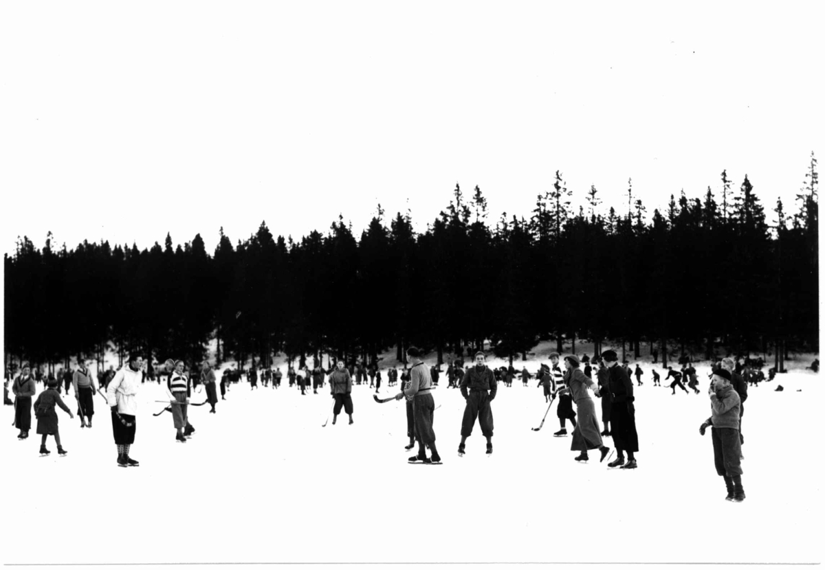 Hermann Christian Neupert, Tryvann skøytebane, 1934. Skøyteløpere i sving på isen. Noen med bandykøller.