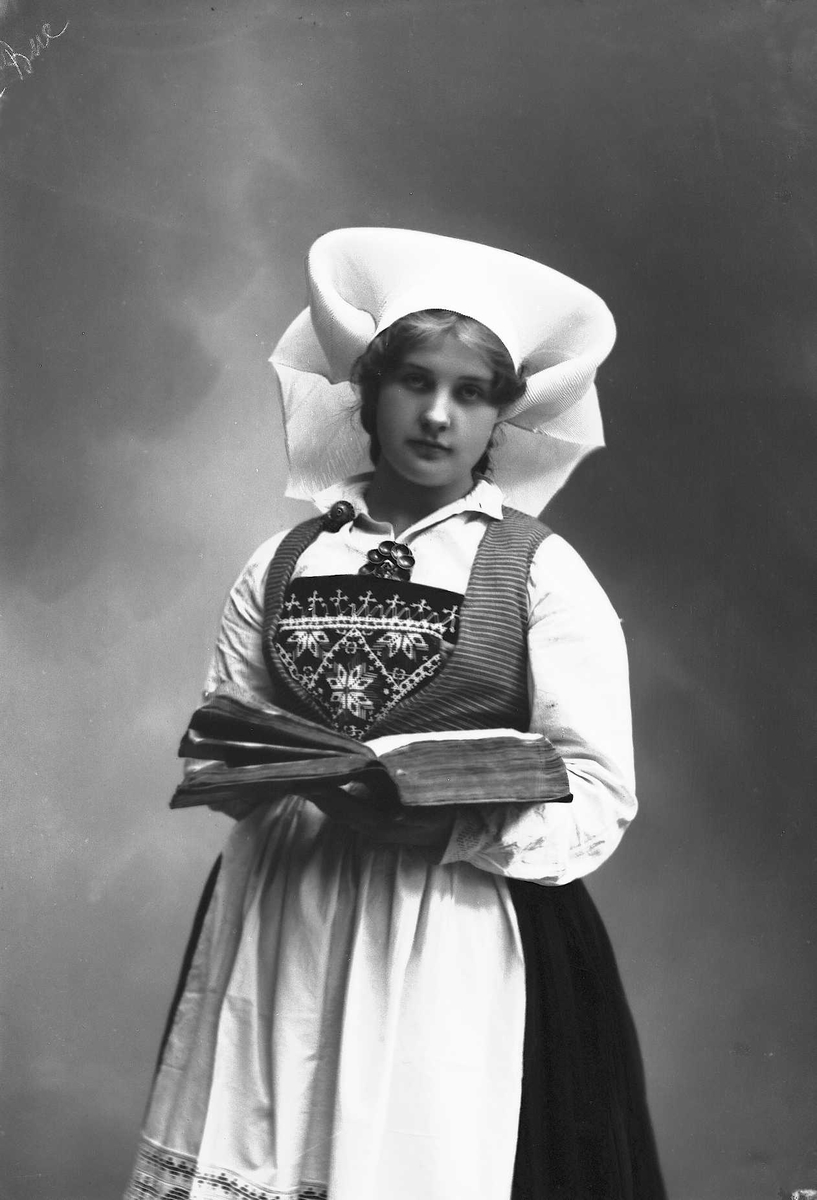 Solveig Lund, Studioportrett av kvinne i drakt og skaut. Hun holder en oppslått bok hendene. Bakgrunnen er nøytral.
