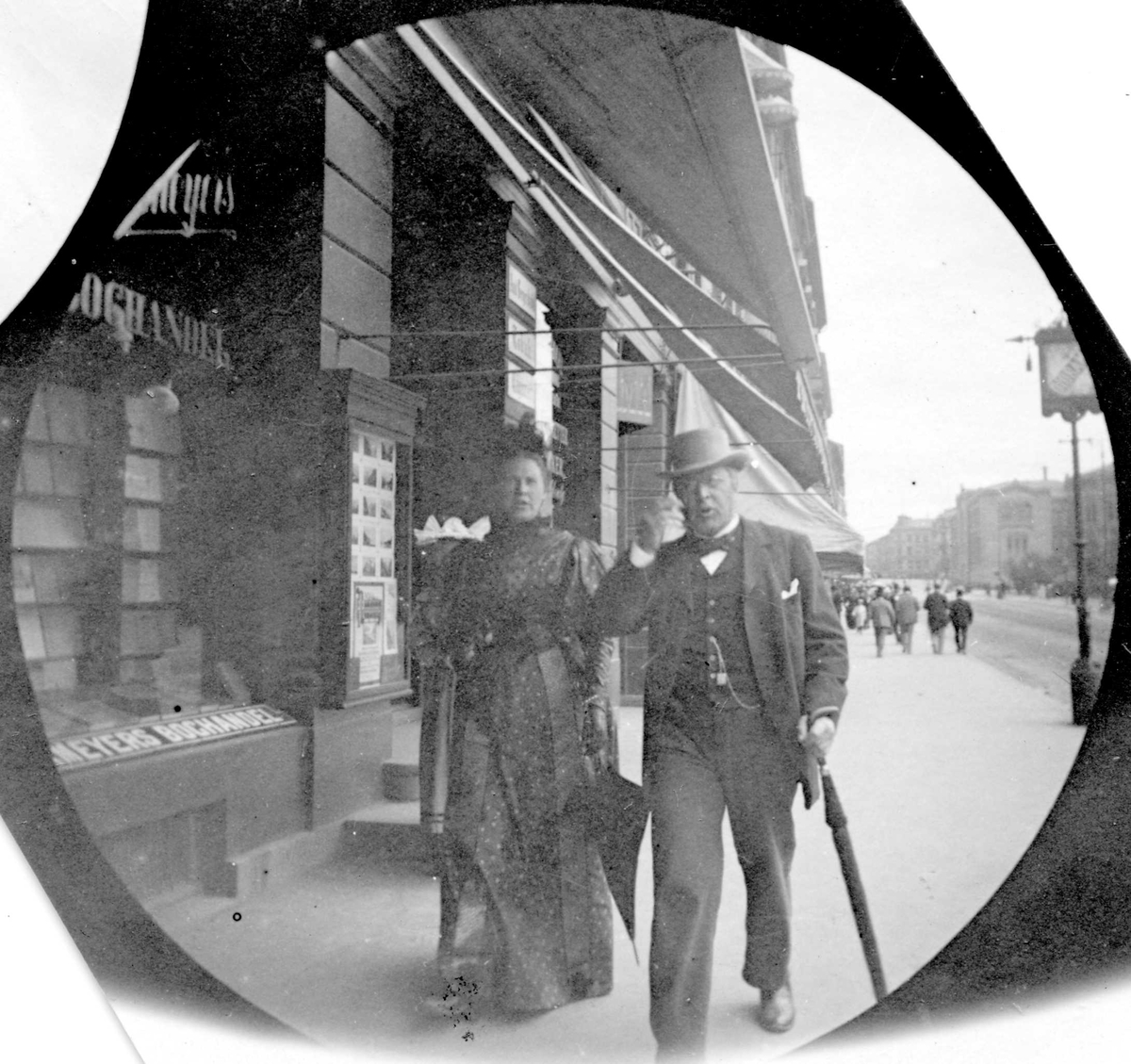 Fredrik Carl Mülertz Størmer, Assessor Reimers og frue spaserer på Karl Johans gate, Oslo, ved bokhandel.
