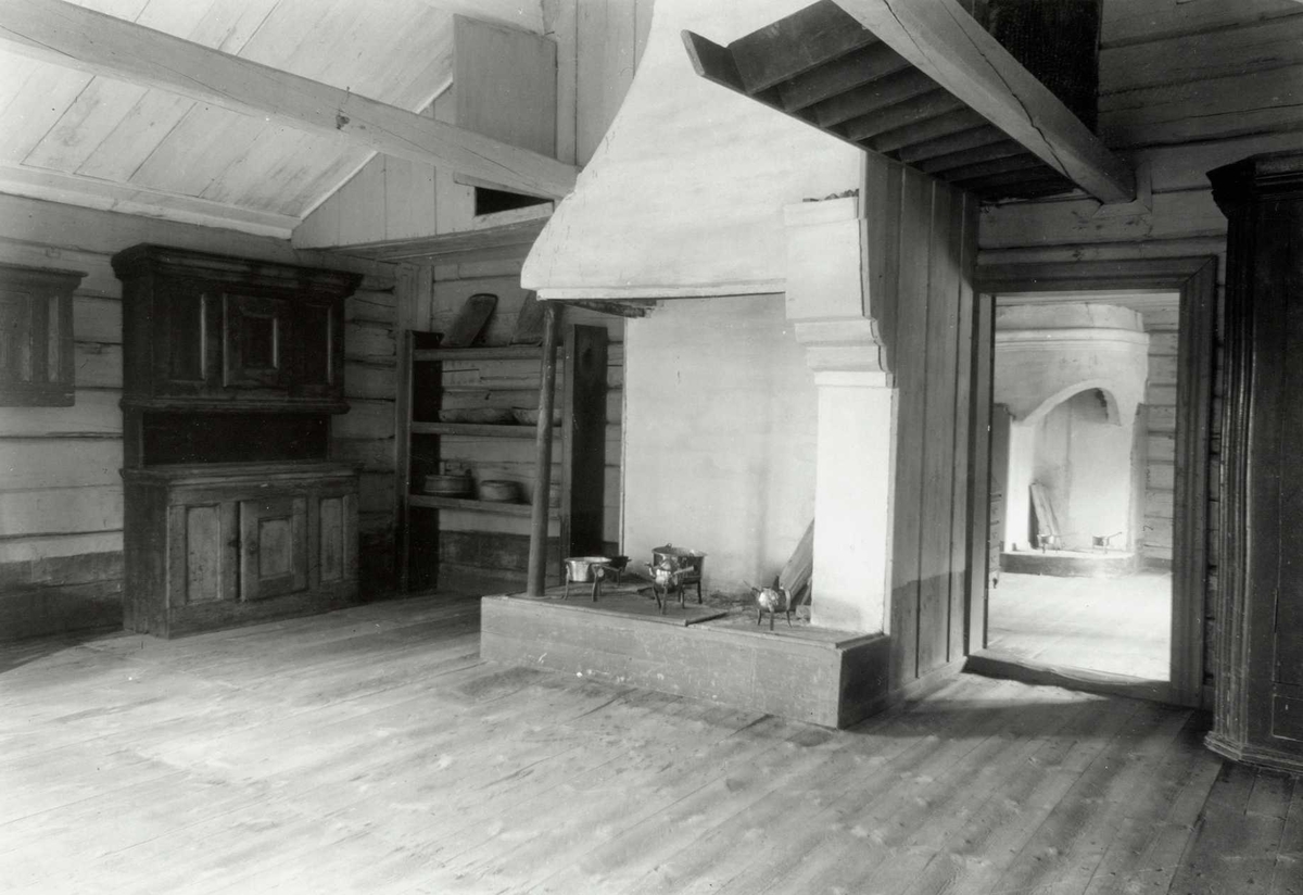 Gisle Midttun, Lømo, Elverum, Sør-Østerdal, Hedmark. Interiør fra stue med peis, kobberkjeler, skap, hyller og bord. Dør til et annet ron med en peis til. Nå på Glomdalsmuseet.