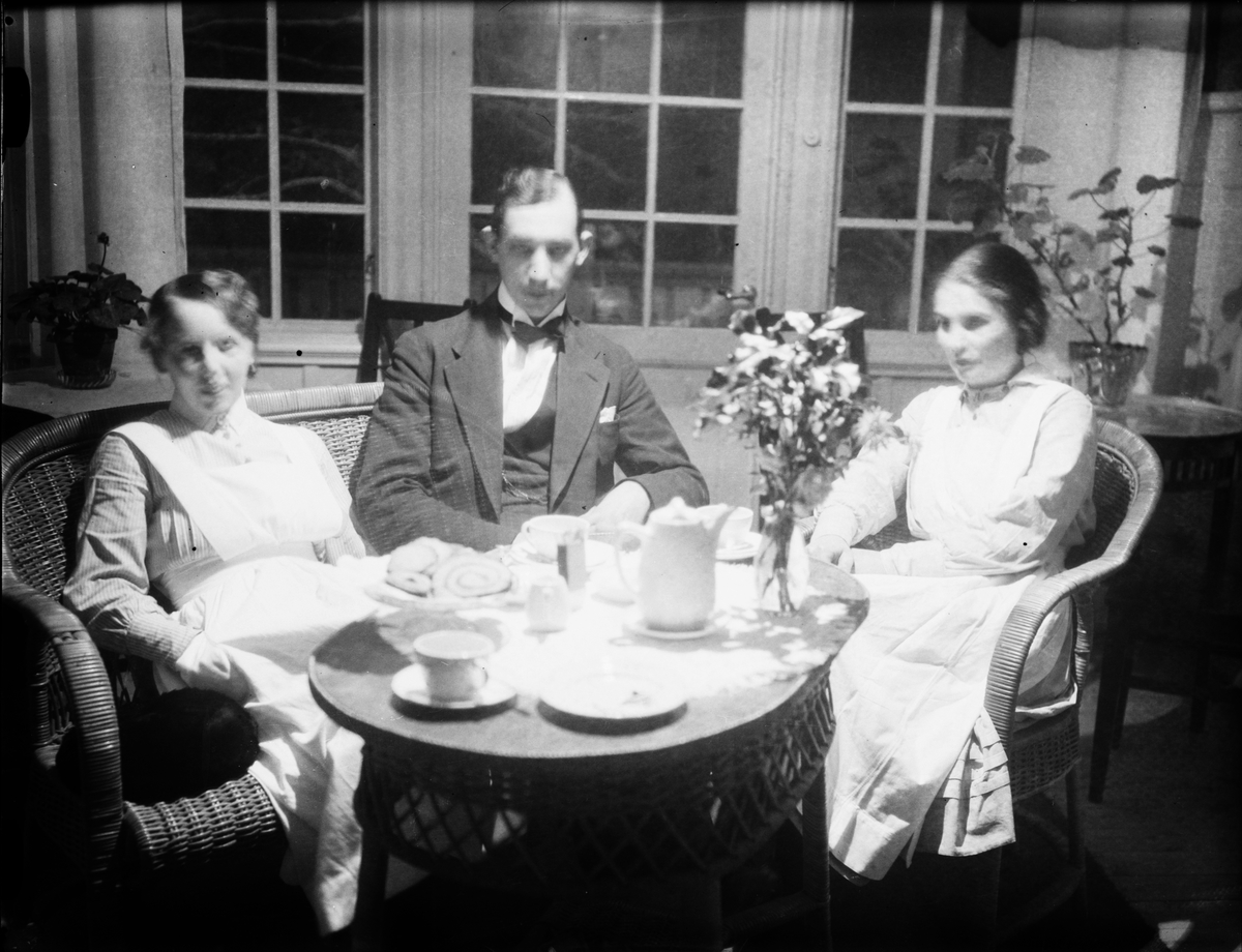 Skötsner-Edhlund, Josef Edhlund sitter vid kaffebordet tillsammans med två kvinnor klädda i sjukvårdsuniform, Östhammar, Uppland