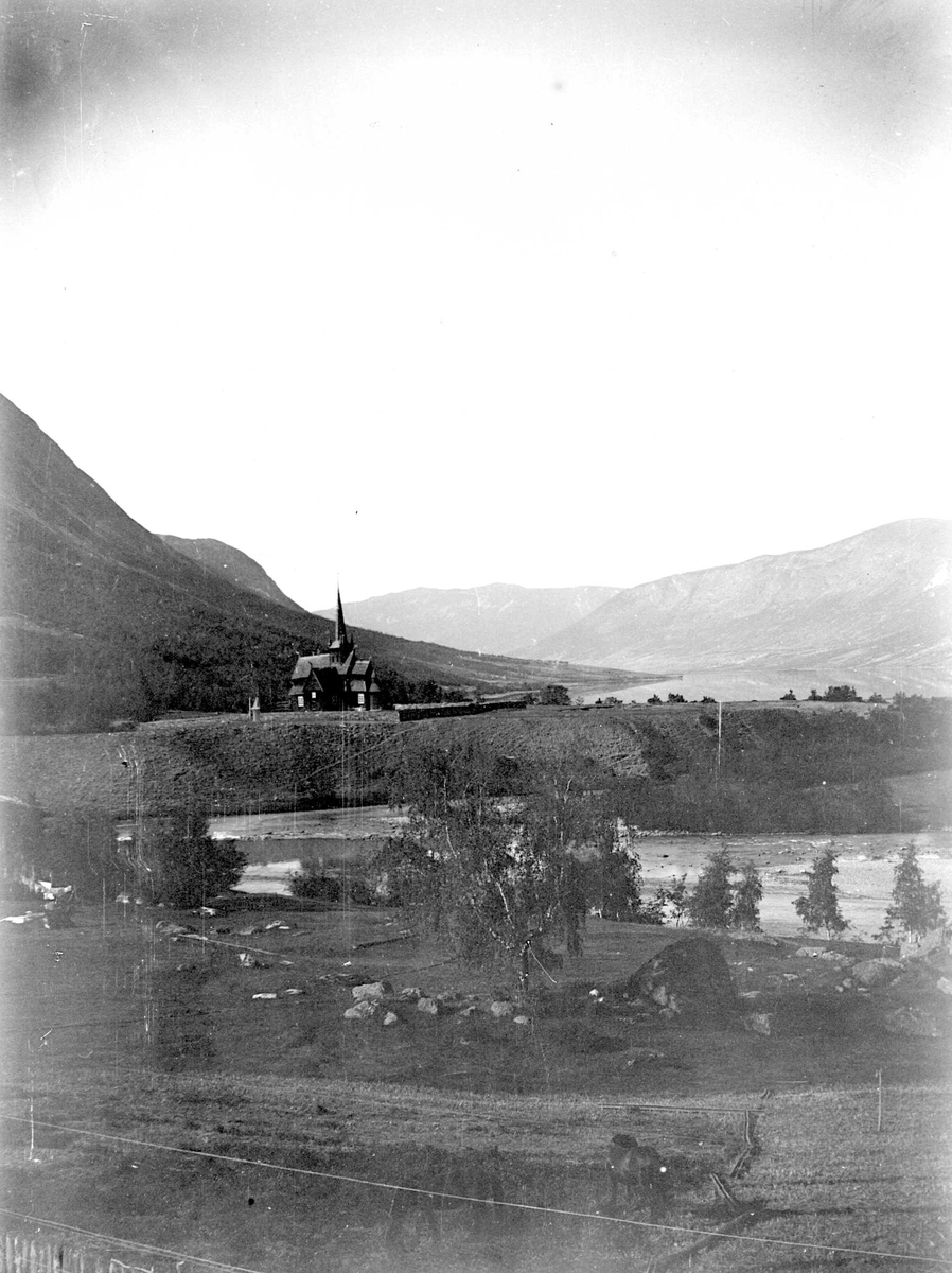Juliane Fredrikke Langberg, Landskap, ukjent sted (norsk) med kirke, fjell og fjordparti i bakgrunnen. I forgrunnen hest på beite(?). Fra malerinne Juliane Fredrikke Langbergs (1856-1930) samling, tatt ca.1895-1910 med motivkrets slekt og venner samt steder tilknyttet samvær med disse.