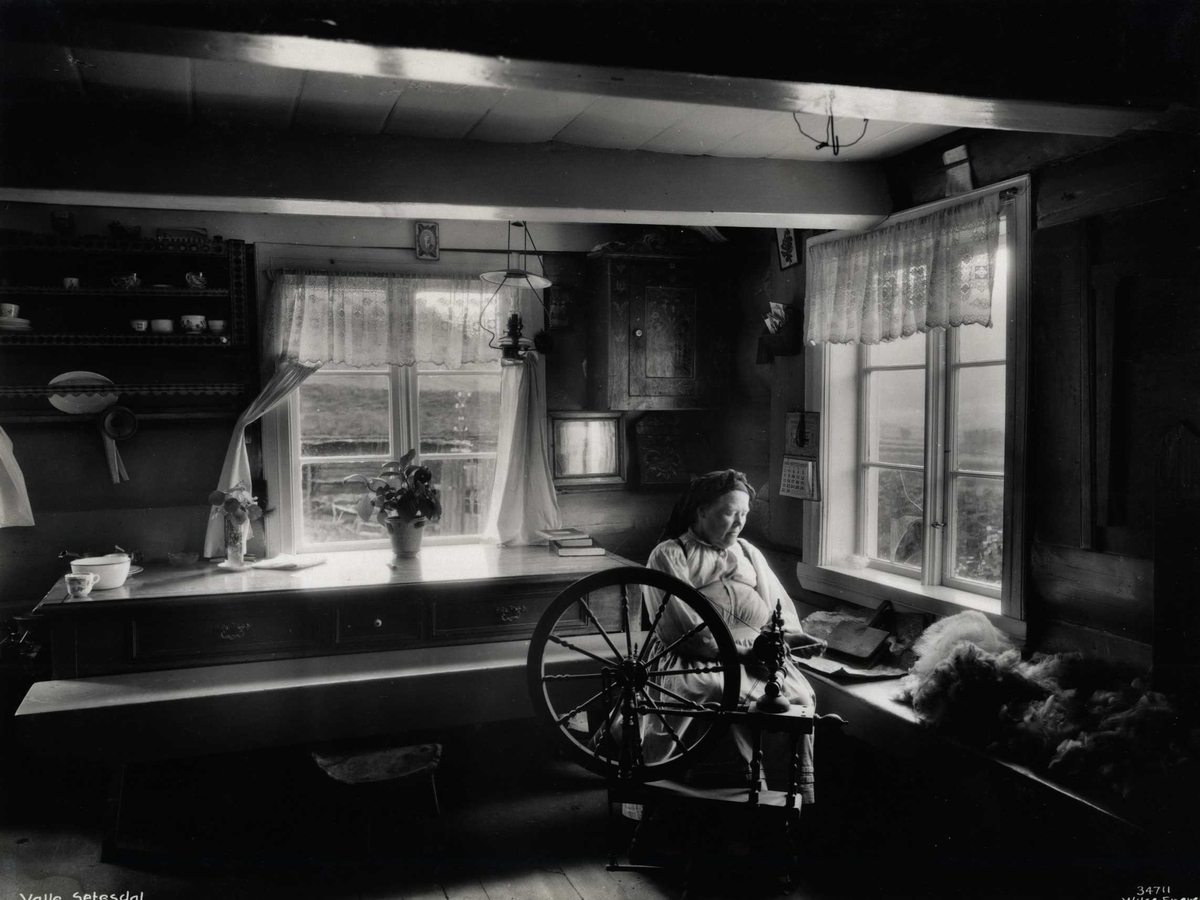 Anders Beer Wilse, En kvinne spinner på rokk i en stue. Valle, Setesdal, Aust-Agder, antagelig 1929.