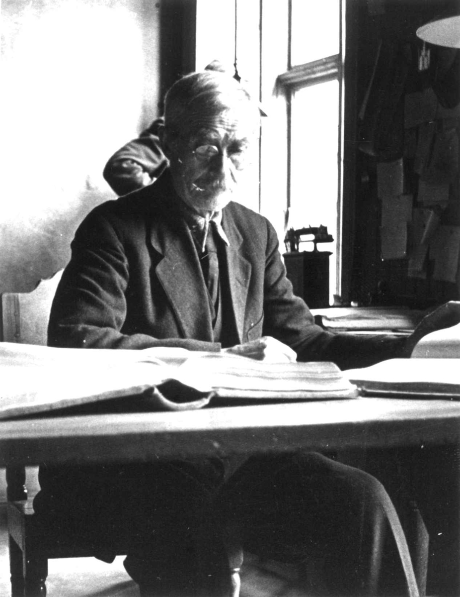 Anna Grostøl, Bokholder Jon Skræddar i Hjorts Stiftelse sitter ved skrivebordet, i bakgrunnen står en gammel telefon. Røros, Sør-Trøndelag 1938.