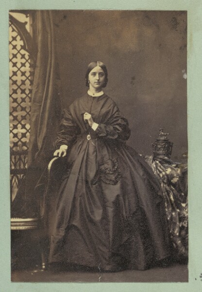 Unknown, [Portrait of young woman standing next to chair]