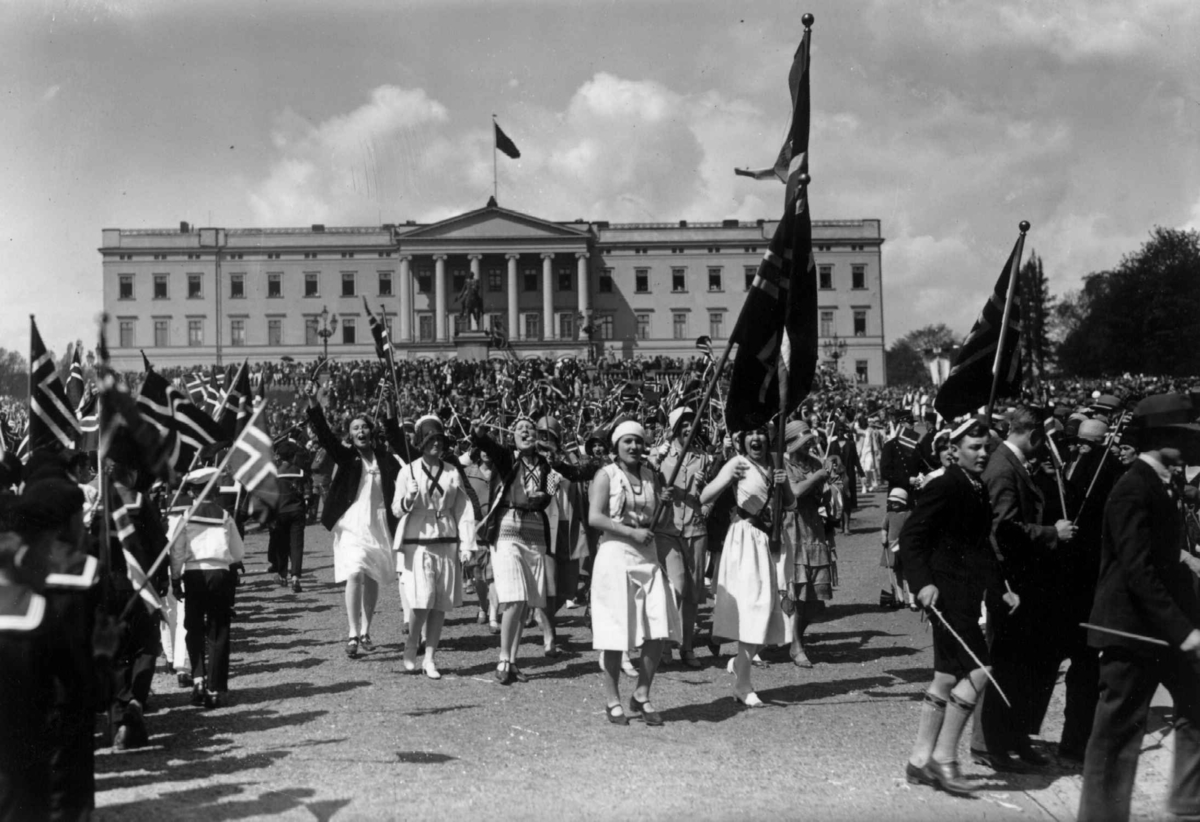 Hermann Christian Neupert, 17. mai-tog på Slottsplassen. Barn med flagg på vei opp mot slottet. Ungom med flagg og faner på vei ned mot Karl Johan. Slottet i bakgrunnen.