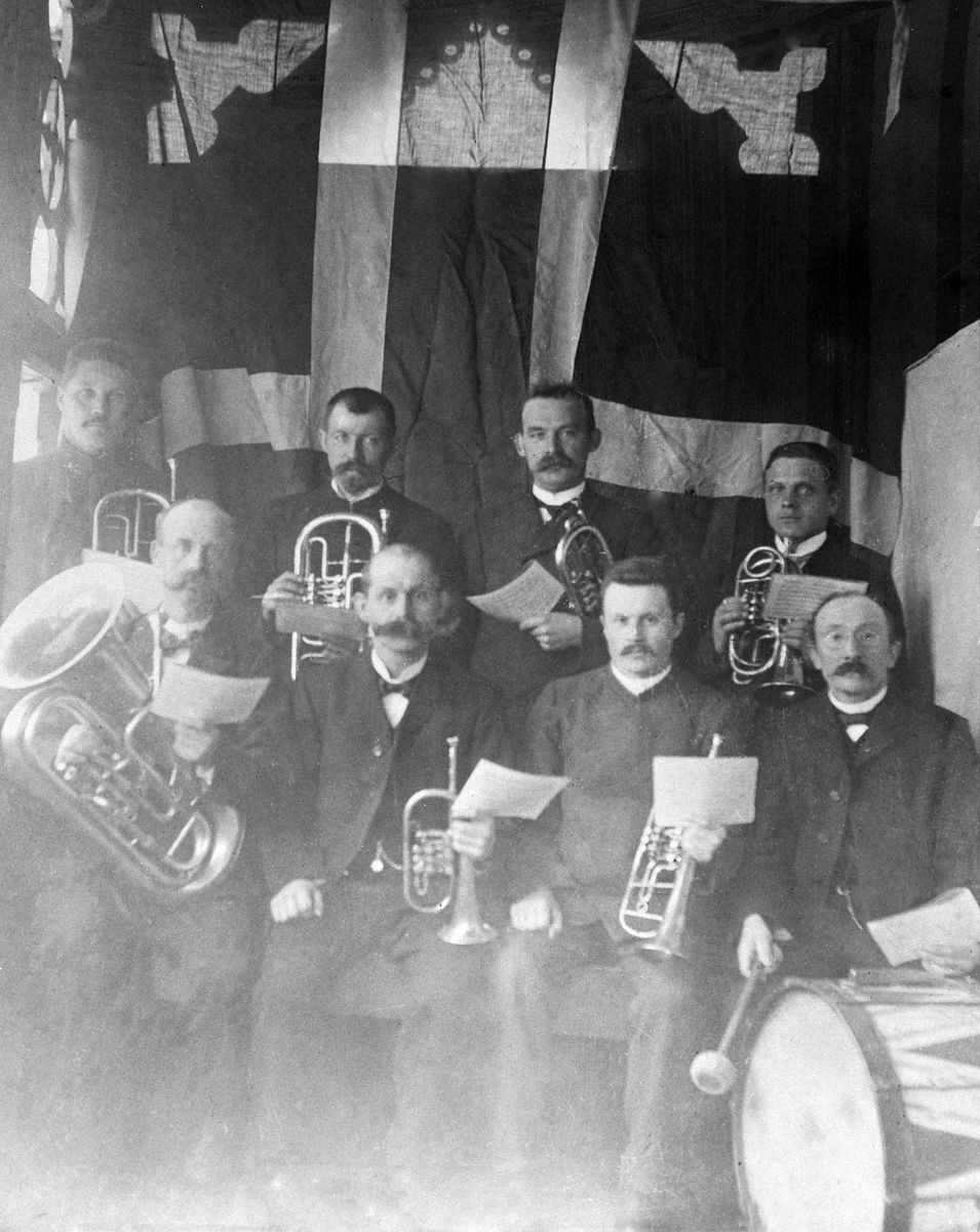 Ukjent, GR: 8 MENN M/MESSINGINSTRUMENTER OG STORTROMME, AADALS BRUKMUSIKKFORENING, FRA V:JAN JENSEN, ERIK BERGSTED Lauritz Hauge, Ole Torkildsen, 2 r: Ole Vik, Petter Torkildsen, Andreas Mikkelsen, Anton Nilsen.