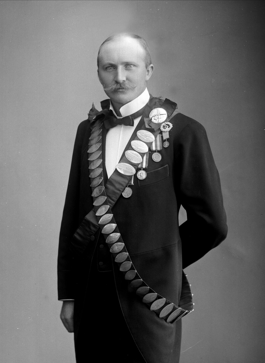 Gustav Borgen, Portrett av Peder Olaf Olsen, antakelig. Bånd med premieplaketter fra skyting. Kongebeltene til Skydeselskapet Skarpskytten. Ingeniør P Olsen, vinner i 1904(?). Den avbildede kan være P. Olaf Olsen, f. 1871 i Drammen, ingeniør ved Den norske fiskegarnsfabrik.