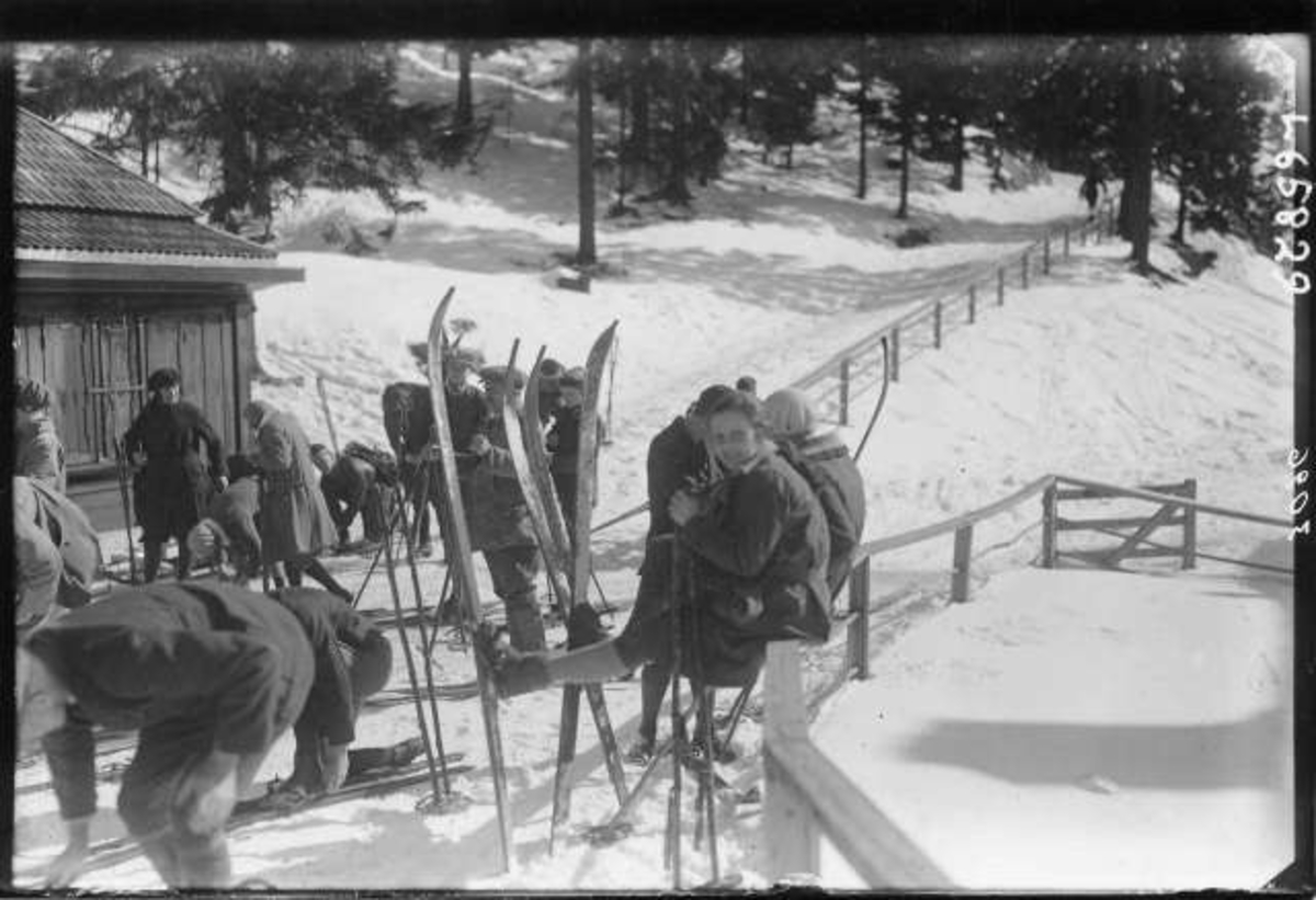 Hermann Christian Neupert, Skiløpere samlet utenfor skihytte i marka. Noen sitter på gjerdet, andre tar av eller på ski.