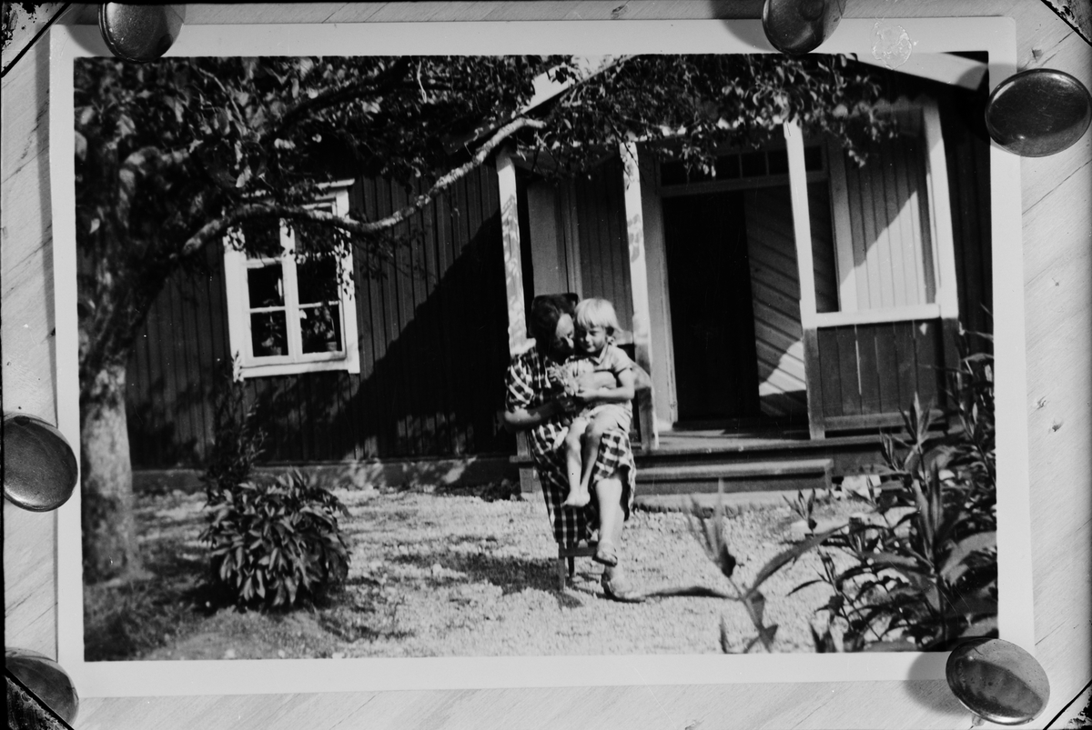 Skötsner-Edhlund, Reprofotografi - kvinna med barn i knät utanför bostadshus, Östhammar, Uppland