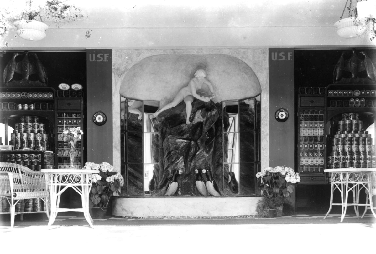 Hermann Christian Neupert, Jubileumsutstillingen på Frogner, Oslo, 1914. Interiør paviljong. Skulptur og reklame. Skulptur midt på bildet. På hver side av denne reklameprodukter.