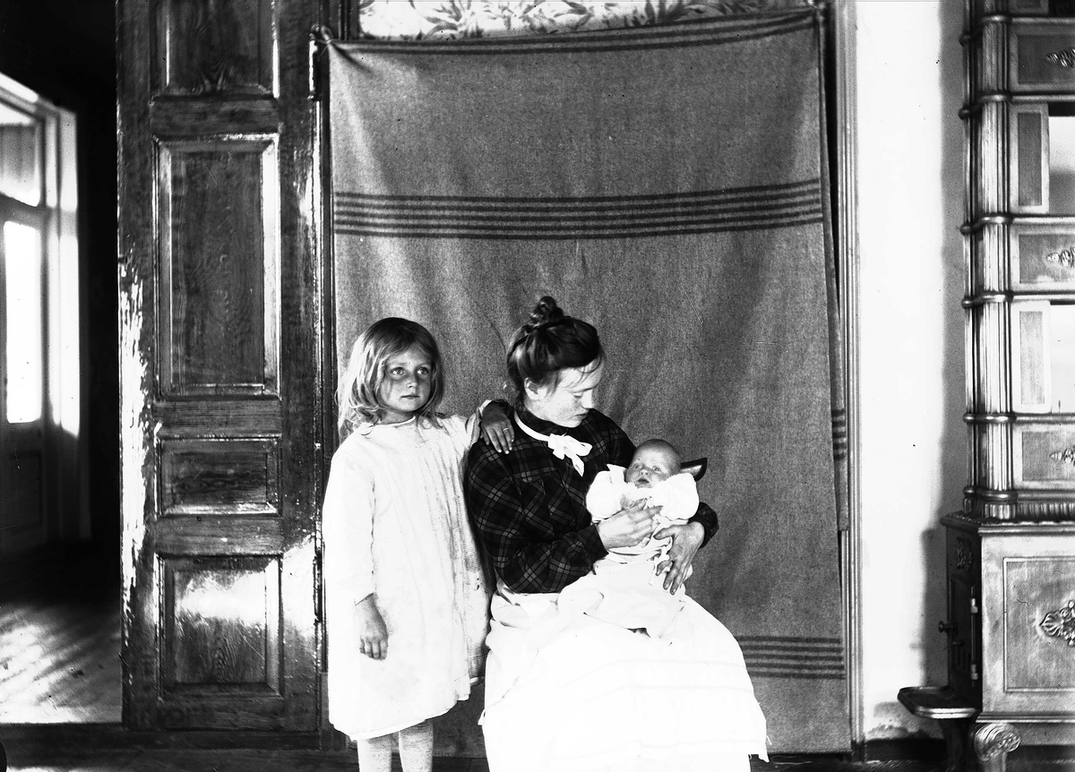 Axel Quinsgaard Wiborg, Interiør, Nedre Digerud, Frogn, Akershus, 1902. Gudrun og Margrethe med Pubben. Fotografert mot opphengt bakteppe.