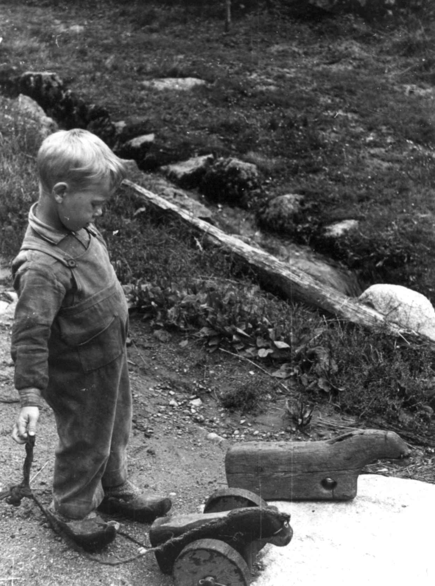 Anna Grostøl, En gutt med en liten hjemmelaget trehest på hjul som han holder i en snor. Eiken 1941.