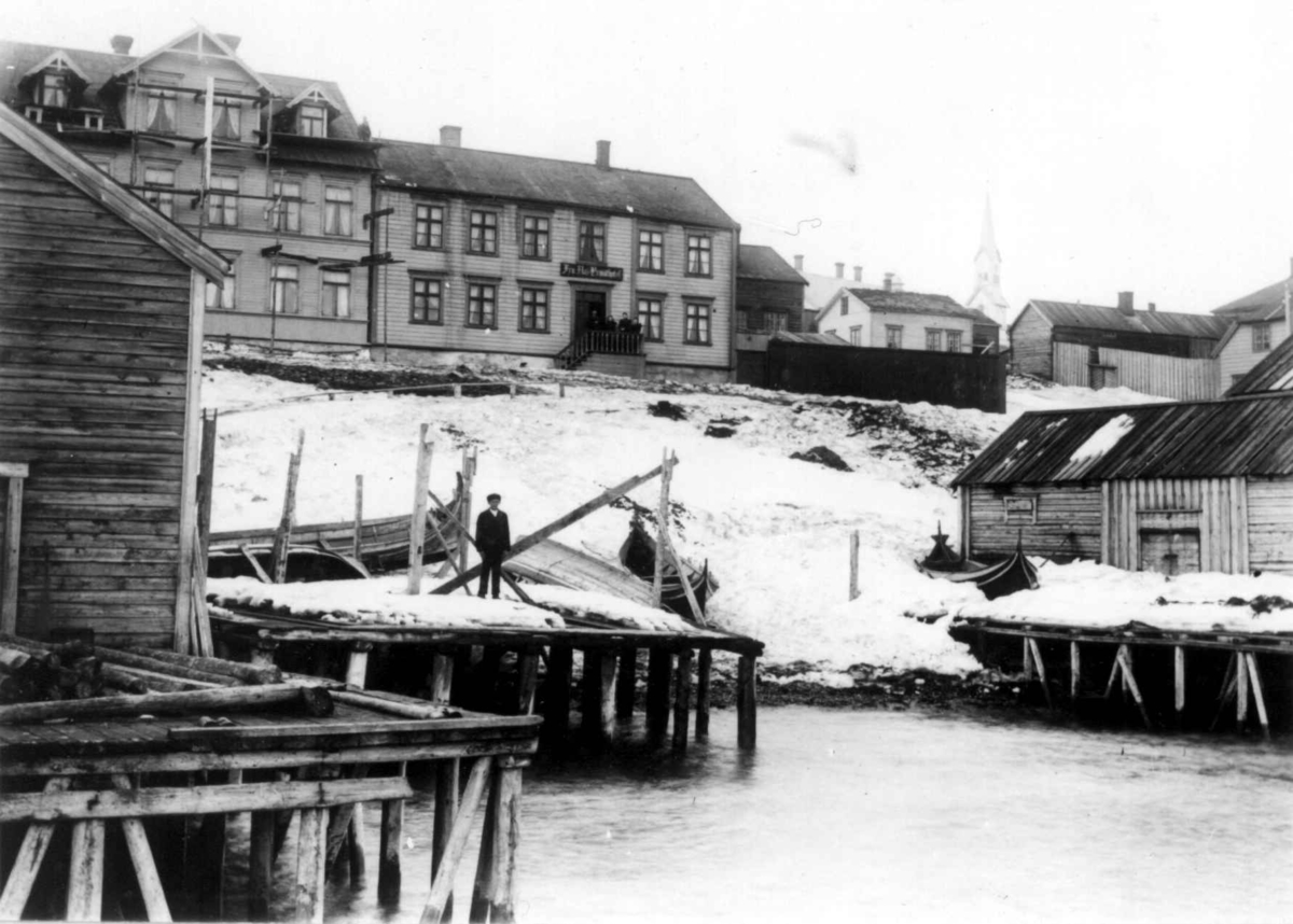 Ellisif Rannveig Wessel, Vadsø, Finnmark. Havneparti med bebyggelse og båter trukket opp på land. Fru Aas hotel i husrekken og kirkebygning i bakgrunnen.