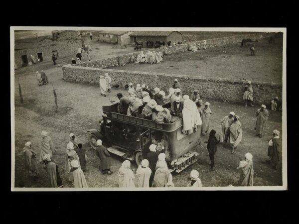 Unknown, Passengers getting onto an already fully-loaded  open-topped bus in Timgad, Algeria.