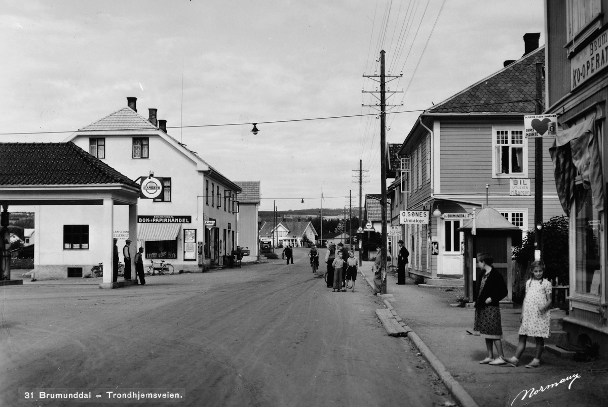 Anno Domkirkeodden, Brumunddal, Furnesvegen, Standard bensinstasjon, Brumunddal Bok og Papirhandel, Urmaker O. Sønes. Telefonstolper. Slutten av 1930-åra. Postkort. 31. Brumunddal-Trondhjemsveien. Foto Normann. Enerett Brumunddal Bok og Papirhandel..