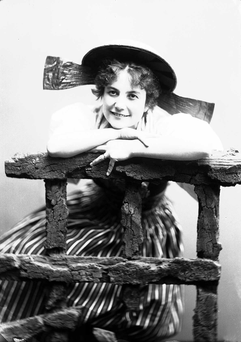 Solveig Lund, Kvinne i drakt og hatt, som lener seg på tregjerde.