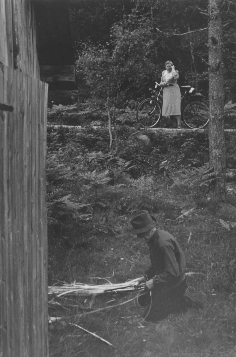 Anna Grostøl, Gunder Tarjeisen Torsland lager bastetau. En kvinne med sykke i bakgrunnen. Åseral 1943.