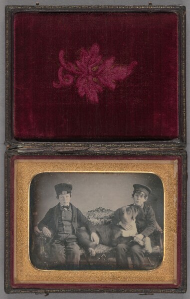 Unknown, [Portrait of two boys wearing caps seated on sofa with a dog]