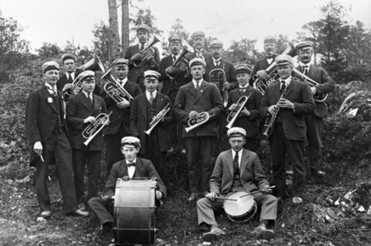 Anno Domkirkeodden, Moelv Musikkforening, 1922, stor gruppe med instrumenter. Foran fra venstre er Aksel Johansen med stortromme, Aksel Sveen med skarptromme. 2. rekke fra venstre er dirigent Peter Nyhus, Ole Hagen, Alf Ødegård, Lars Peersen, ukjent, Ludvig Rosenborg, Aksel Schjerpen og Hans Rosenborg. Bak fra venstre…
