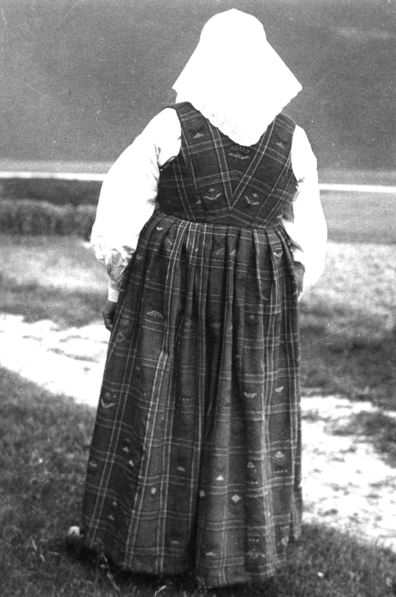 Anna Grostøl, Antagelig Lesja, Oppland 1934. Kvinne i drakt står med ryggen til.
