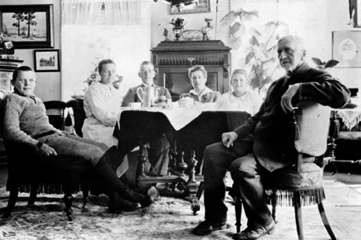 Anno Domkirkeodden, Interiør stue, Kise Mellom, Nes, Hedmark. Gruppe rundt kaffebordet. Fra venstre er Even Arnt Haugen (1909-1962), Maren, Einar Walby, Halvorsen, Anna Marie Kongsrud (1910-1992), Even Arnt Gjestvang (1829-1927).