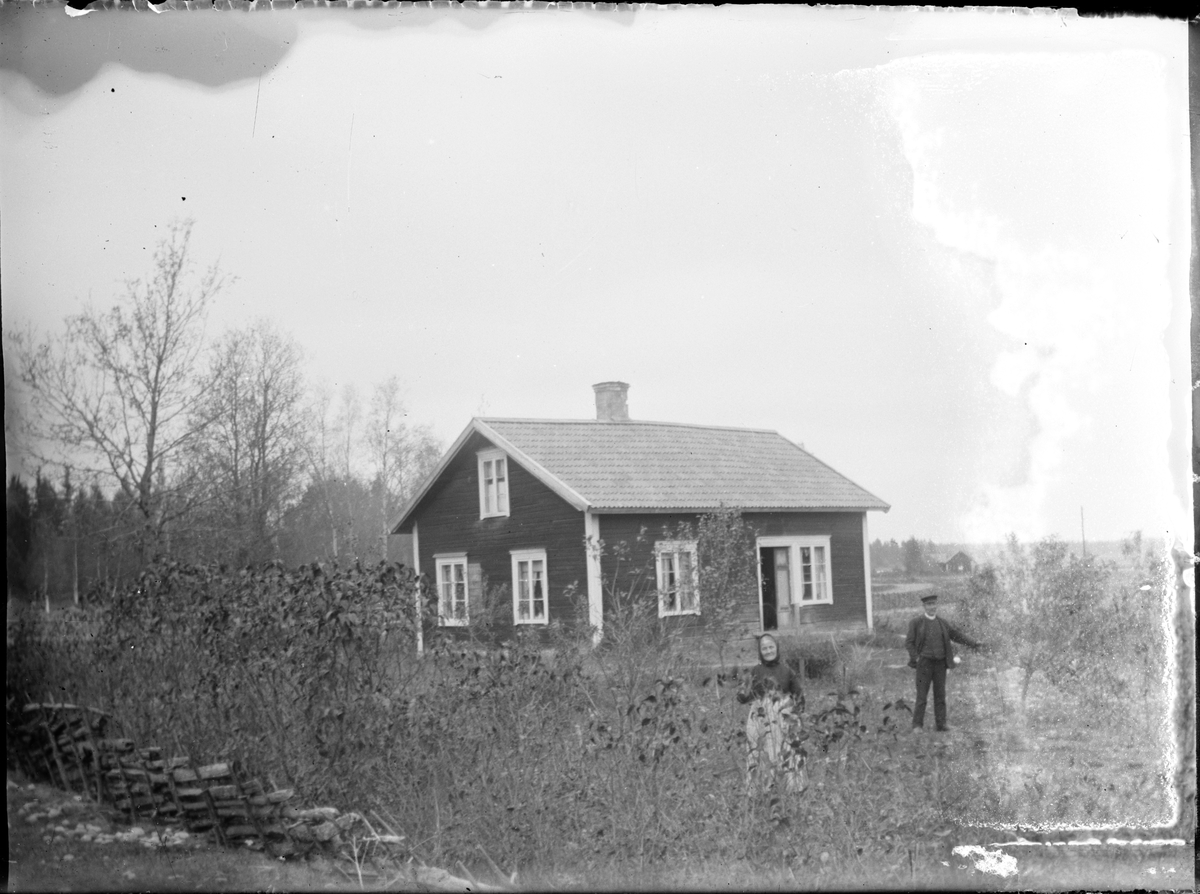 Skötsner-Edhlund, Man och kvinna i trädgården vid bostadshus , Östhammar, Uppland