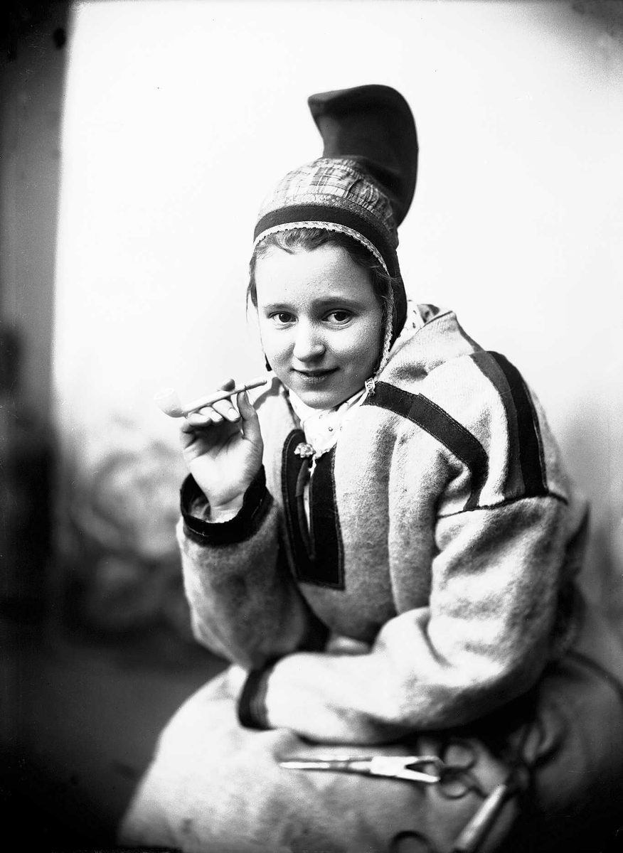 Solveig Lund, Kvinne i sameliknende drakt med kofte, hornlue og pipe. Belte med saks.