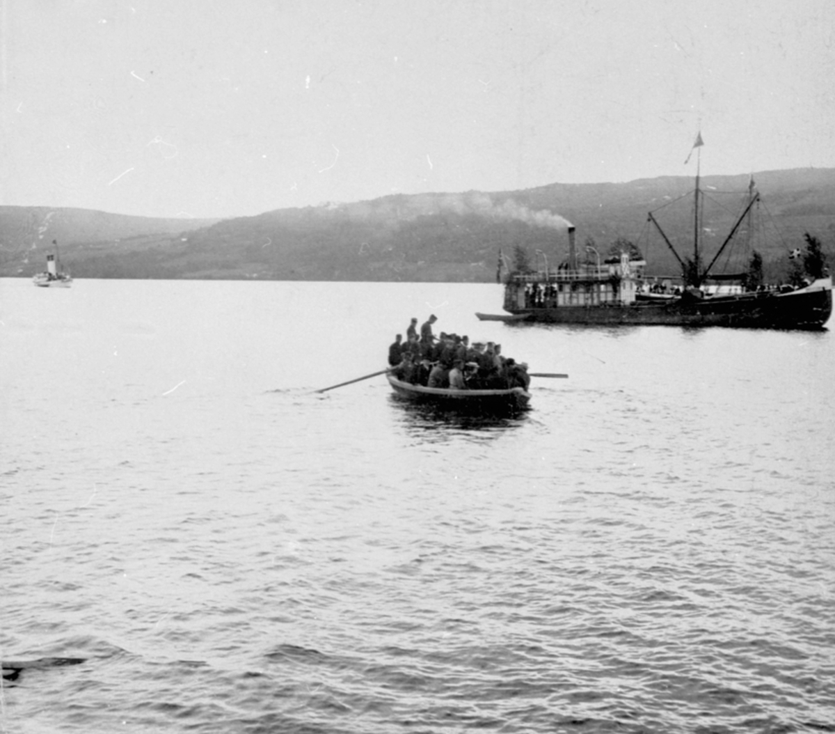 Anno Domkirkeodden, Mjøsbåten D. S. Industri II, pyntet med løv, utenfor Moelv brygge. Robåt full av folk. Kong Oscar i bakgrunnen.