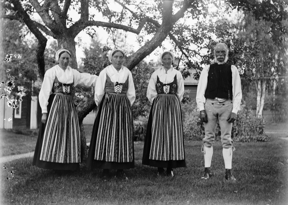 Okänd,, Svens Olle med sina tre döttrar Kristina, Anna och Britta, klädda i folkdräkt, står i trädgården på Svensgården, Dalarna, Sverige 1919