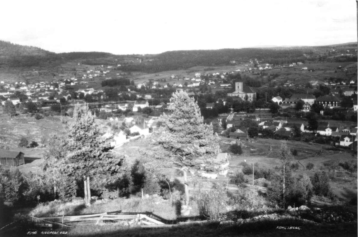 Hermann Christian Neupert, Kongsberg - Buskerud. 1930. Oversiktsbilde. Landskap. Skog rundt byen. Bebyggelse. Kongsberg kirke (1761) i bakgrunnen.